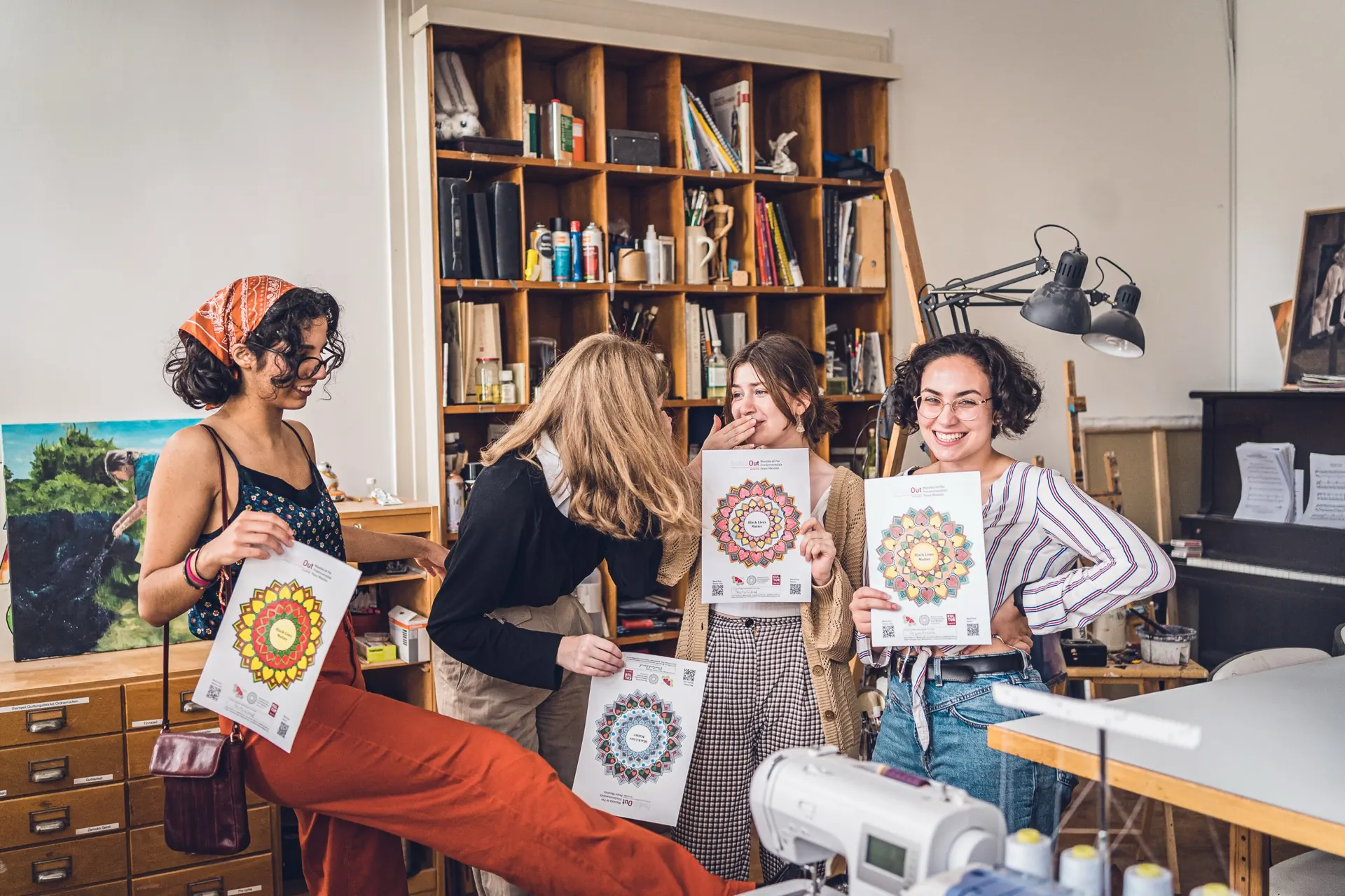 Vier Frauen stehen lachend im Atelier und halten frisch gestaltete Blätter hoch.