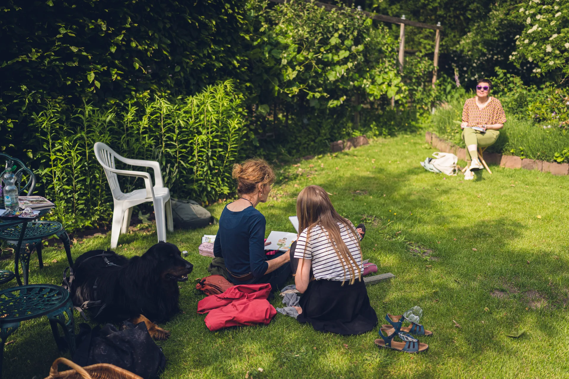 Zwei Menschen zeichnen im Gras, ein Hund liegt neben ihnen.
