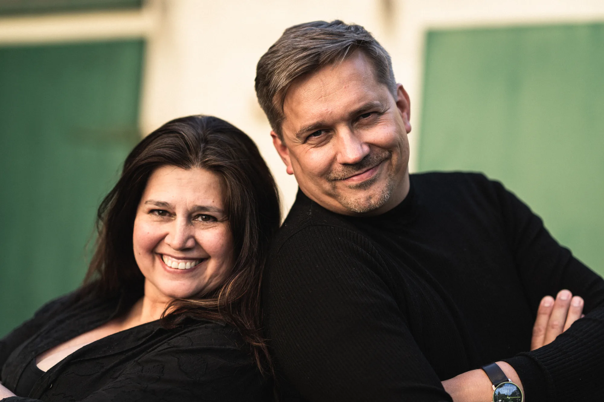 Zandra Gröschner Rico del Valle und Roman Thomas, die Vereinsleitung von Denk.Mal, sitzen Rücken an Rücken und lächeln.